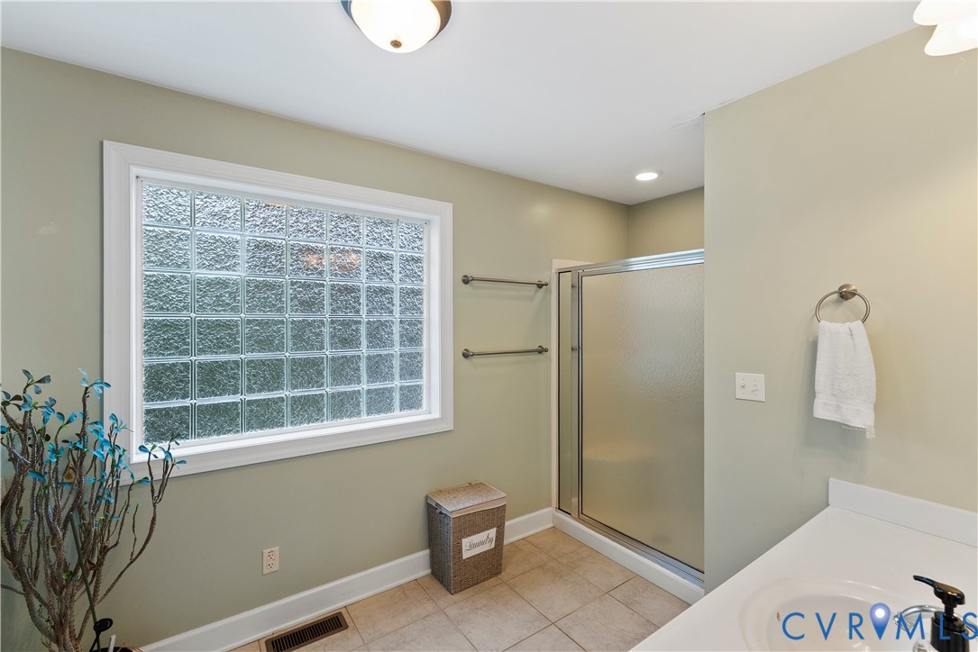 Bathroom featuring a glass block window, walk-in shower with a frosted glass enclosure, tile flooring, and a vanity with a white countertop