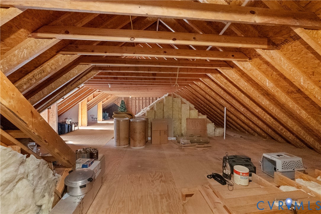 Unfinished attic space featuring exposed wood rafter framing, plywood subflooring, and insulated wall sections