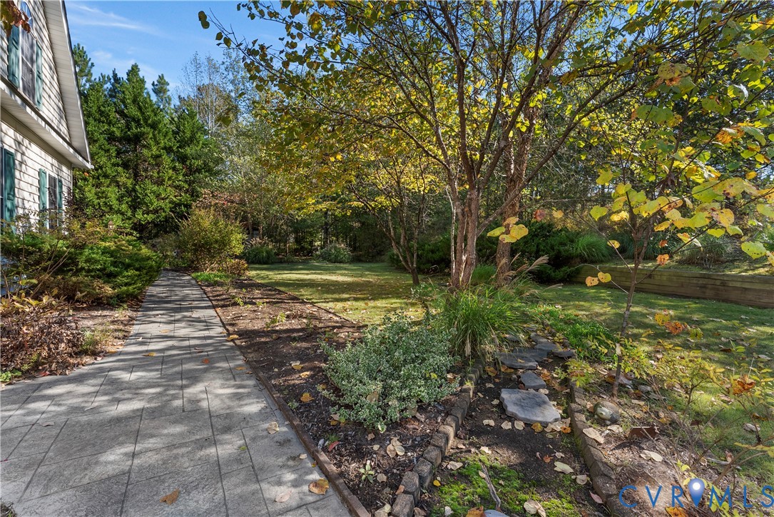 Concrete paver walkway, mature trees, expansive lawn, stone garden edging, and tiered timber retaining wall