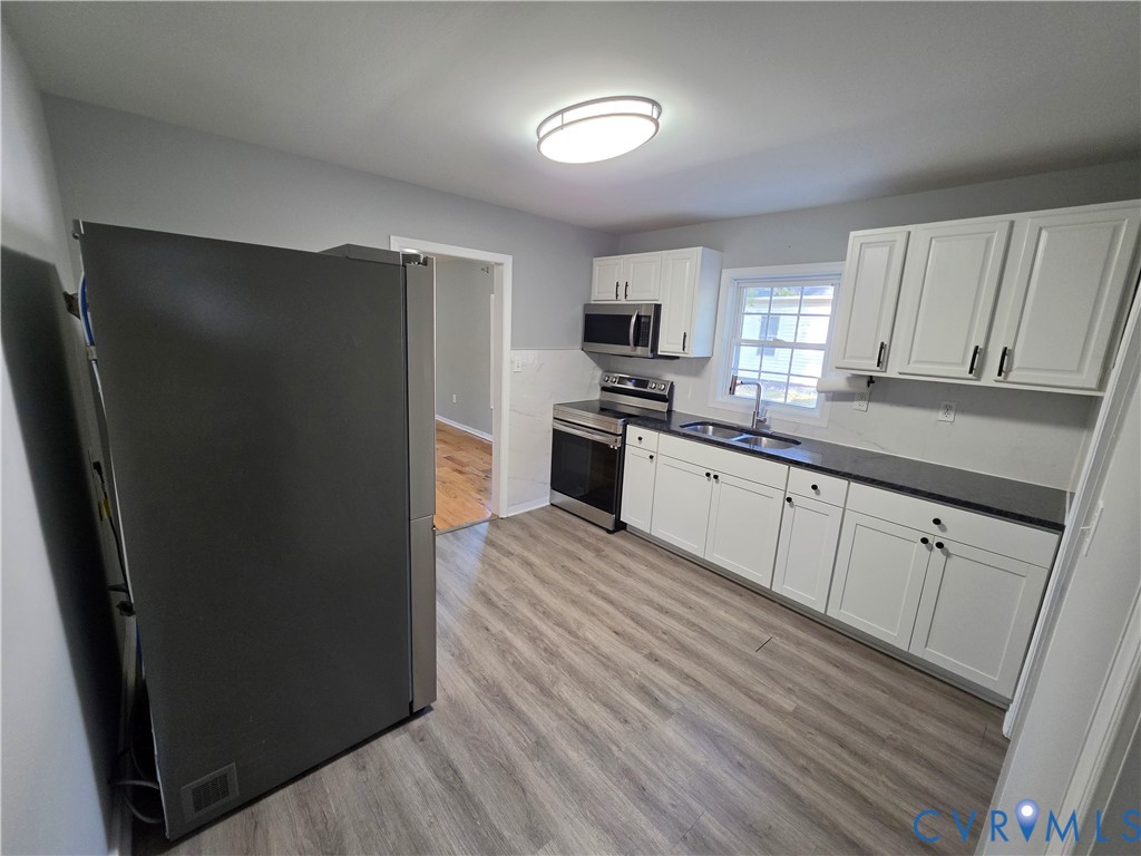 Kitchen featuring white shaker-style cabinetry, dark solid-surface countertops, stainless steel appliances, and wood-finish flooring