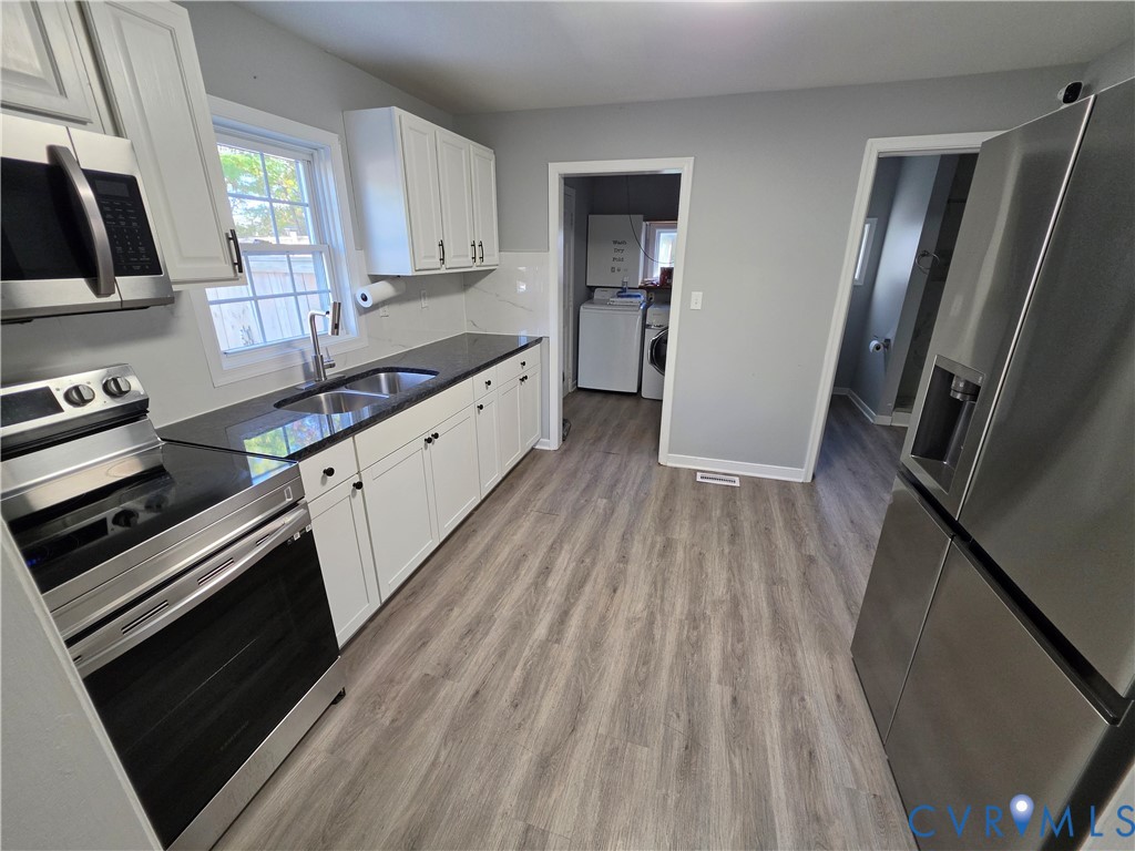 Kitchen featuring white shaker-style cabinetry, stainless steel appliances, dark countertops with a dual-basin sink, and wood-finish flooring