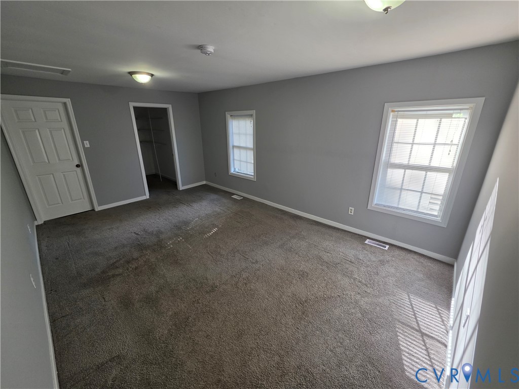 Neutral-toned room featuring wall-to-wall carpeting, two double-hung windows, and a walk-in closet with built-in shelving