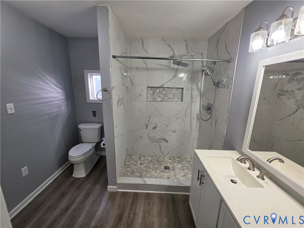 Bathroom featuring wood-finish flooring, a vanity with a white countertop and integrated sink, a walk-in shower with stone-tile surround, and a recessed shower niche