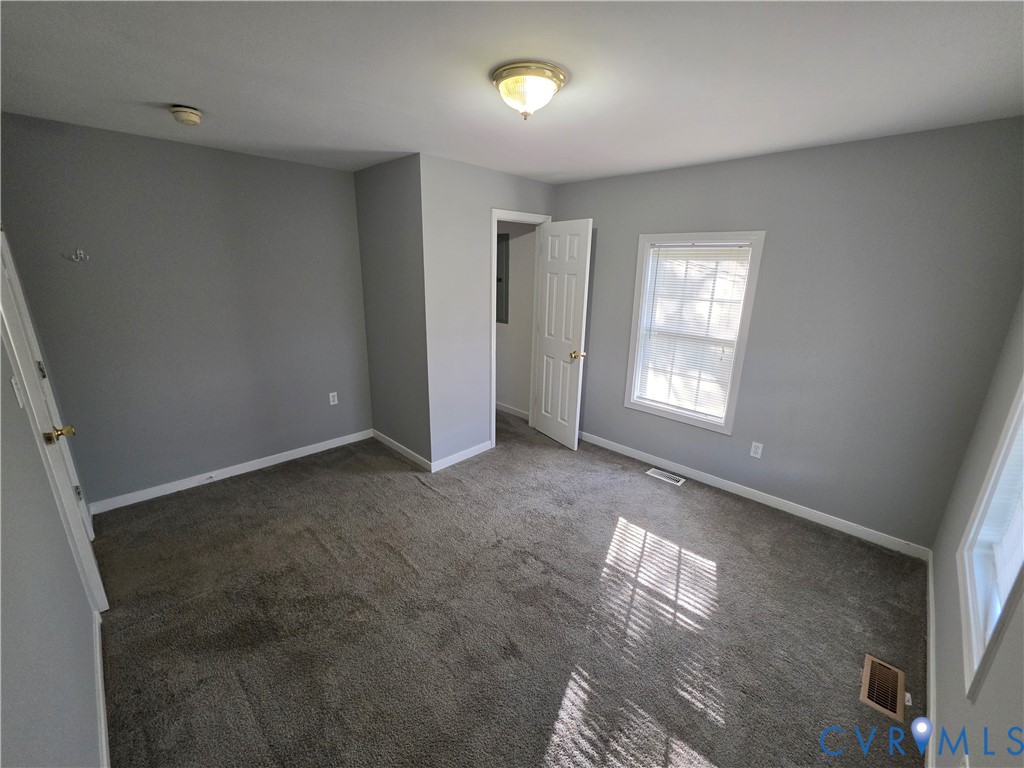 Neutral-toned interior space featuring wall-to-wall carpeting, grey-painted walls, a multi-pane window, and a white six-panel door