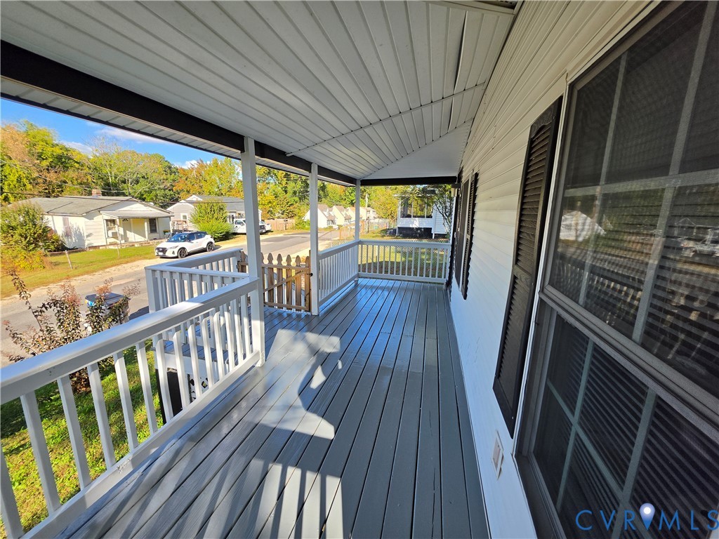 Covered front porch featuring painted wood decking, white baluster railings, and a gated entrance