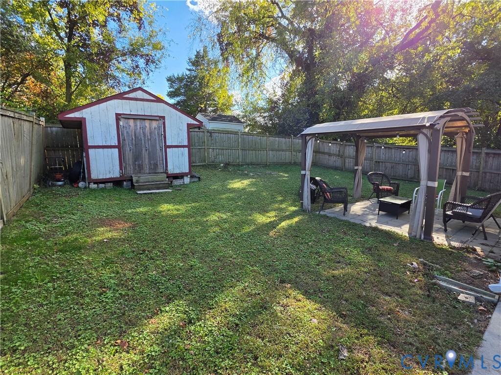 Backyard featuring a wood-sided storage shed, wood privacy fencing, and a permanent metal-frame pergola over a paved patio