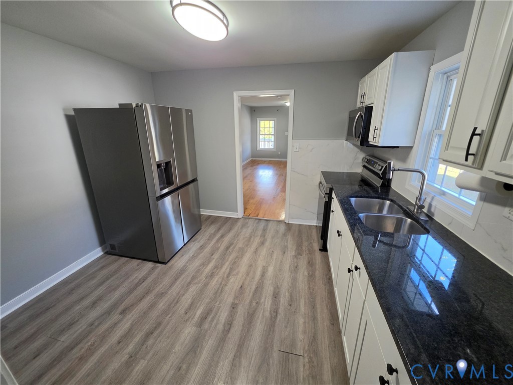 Kitchen featuring stone countertops, stainless steel refrigerator, white cabinetry with matte black hardware, wood-finish flooring, and a double-basin stainless steel sink