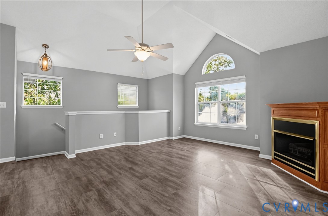 Vaulted ceiling featuring an arched window, wood-finish flooring, fireplace with a wood mantel, ceiling fan with integrated lighting, and decorative pendant lighting