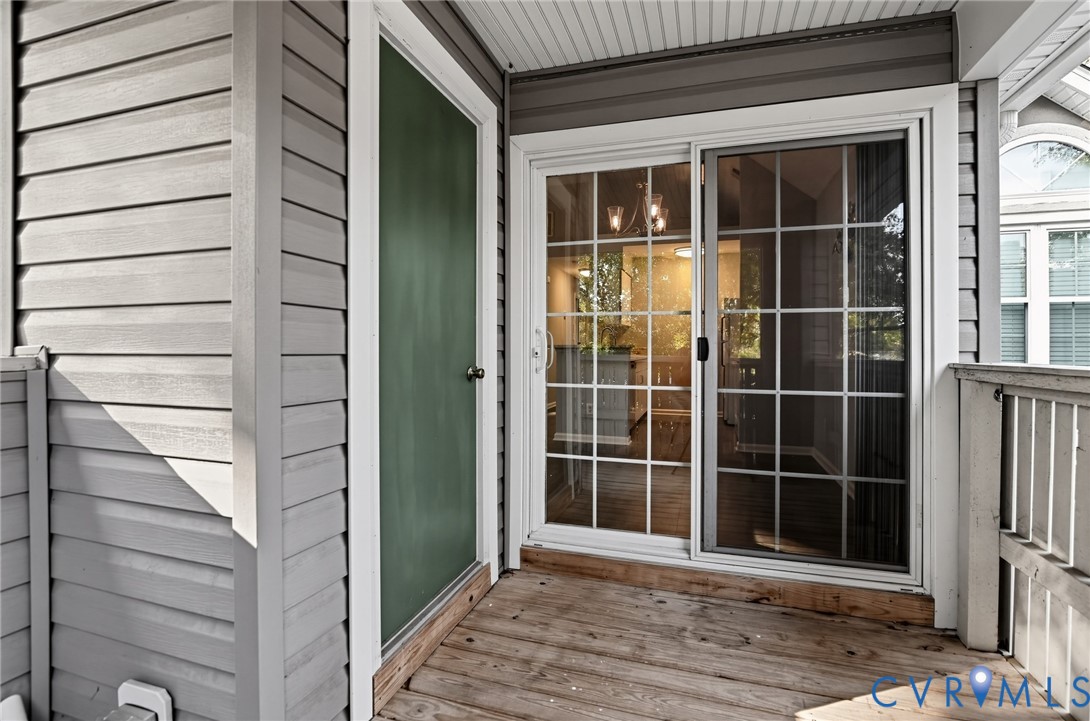 Covered balcony featuring horizontal lap siding, wood-finish decking, and a sliding glass door with a grid pattern