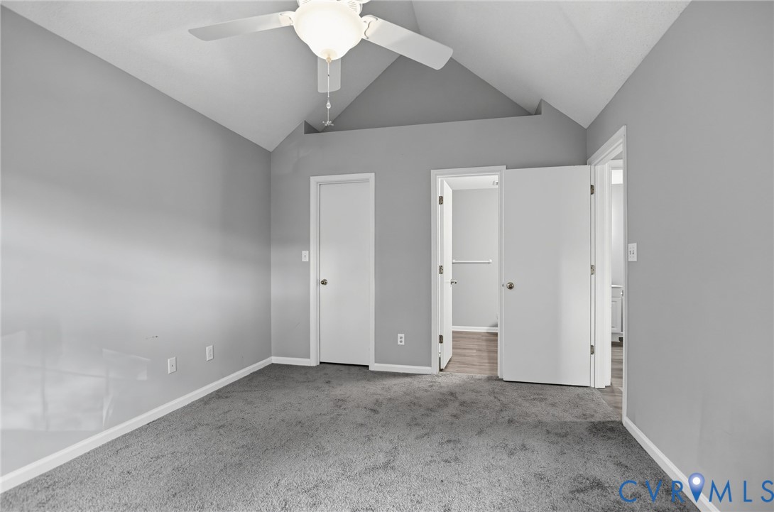 Vaulted ceiling featuring a central white ceiling fan with integrated lighting, neutral wall finishes, and carpeted flooring