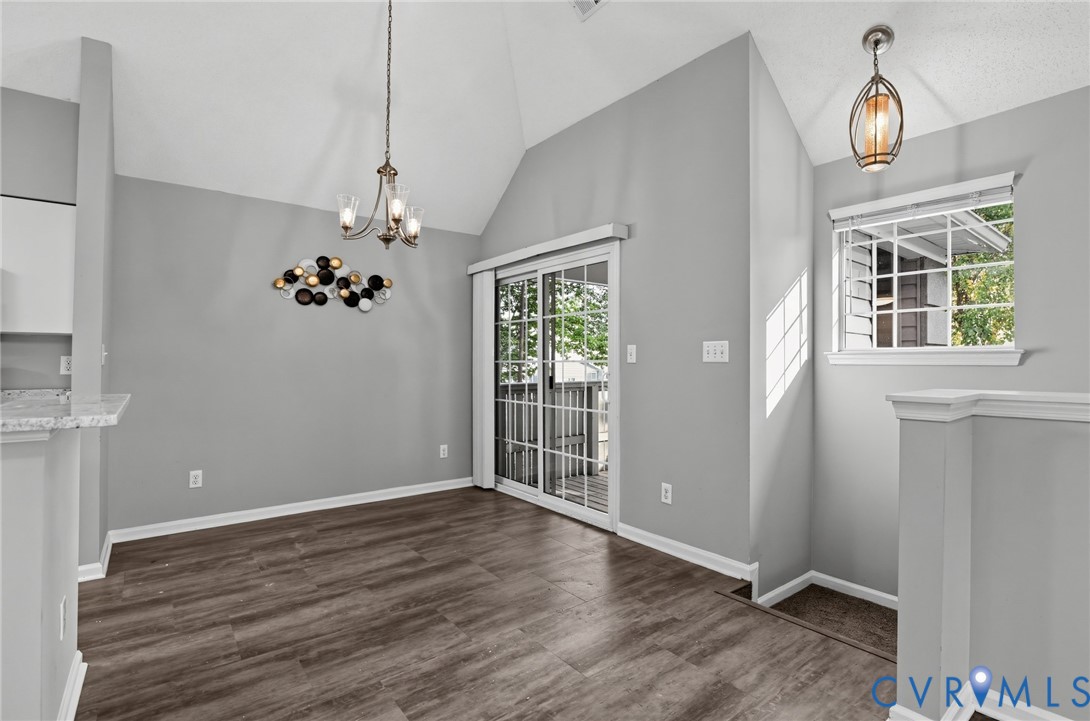 Vaulted ceilings, wood-finish flooring, sliding glass door with external access, and dual pendant lighting fixtures