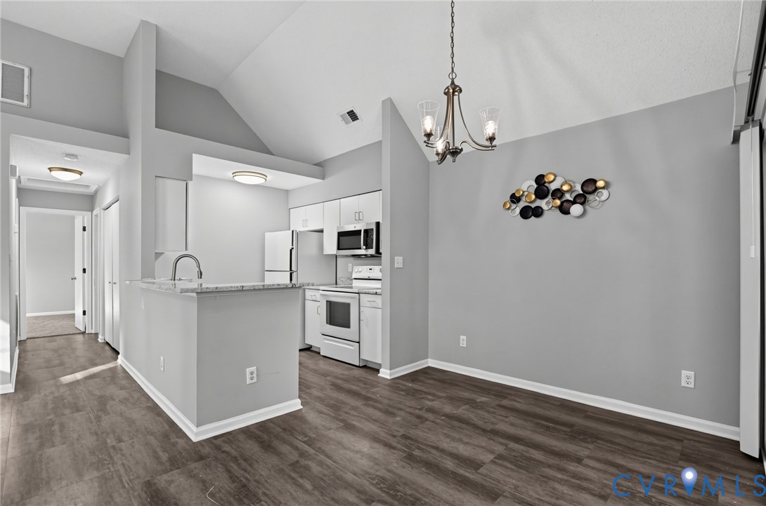 Vaulted ceilings, kitchen featuring white cabinetry, stone-finish countertops, and wood-finish flooring