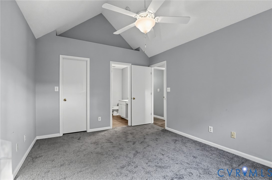 Vaulted ceilings featuring a central white ceiling fan with integrated lighting, neutral wall paint, and wall-to-wall carpeting