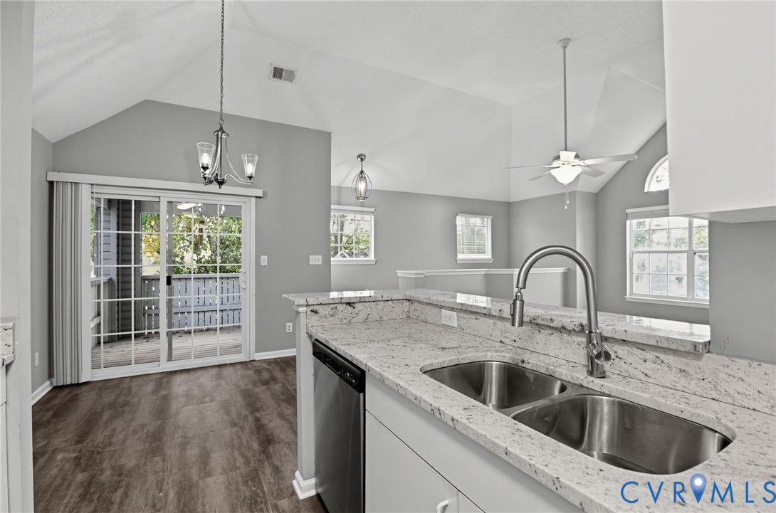 Kitchen featuring stone countertops, a dual-basin stainless steel sink with a high-arch faucet, vaulted ceilings, wood-finish flooring, and sliding glass doors