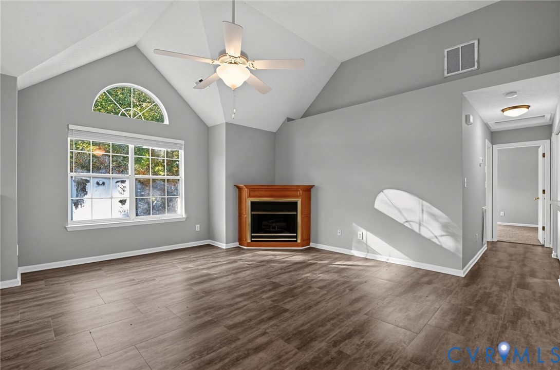 Vaulted ceilings featuring an arched window, wood-finish flooring, and a corner fireplace with wood-tone surround and built-in ceiling fan