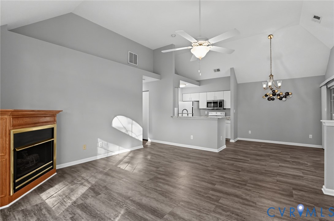 Vaulted ceilings with a ceiling fan, wood-finish flooring, and a fireplace with a wood mantel