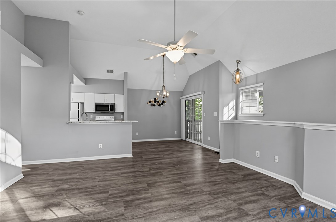 Open concept living area featuring vaulted ceilings, wood-finish flooring, a ceiling fan with integrated lighting, and a breakfast bar overlooking the kitchen