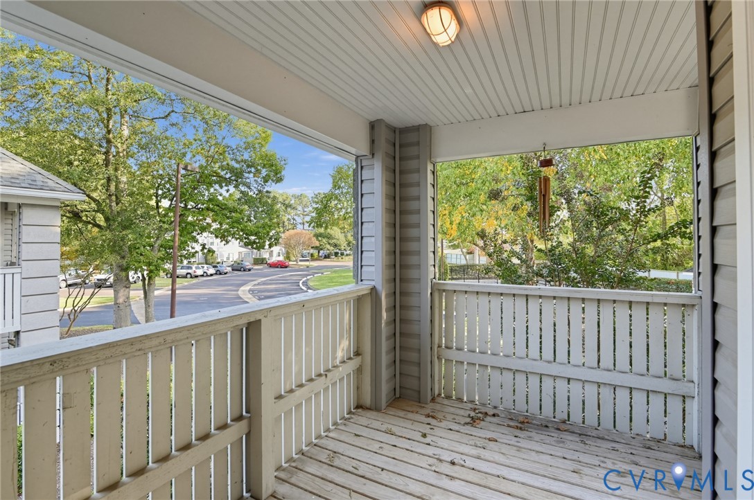 Covered porch with wood decking, horizontal slat railings, beadboard ceiling, and flush-mount exterior lighting