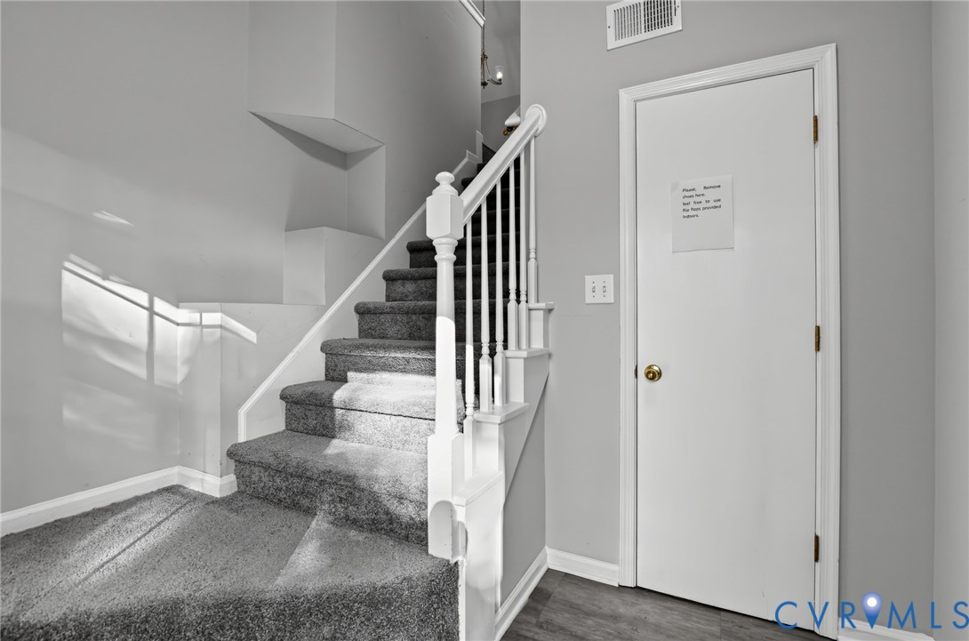 Staircase featuring a white wooden balustrade and neutral-toned carpeting, complemented by a solid core door and wood-finish flooring