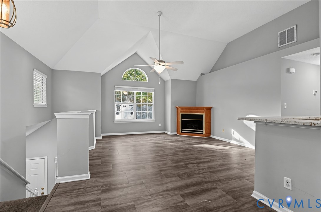 Vaulted ceiling, wood-finish flooring, corner fireplace with wood mantle, and arched window