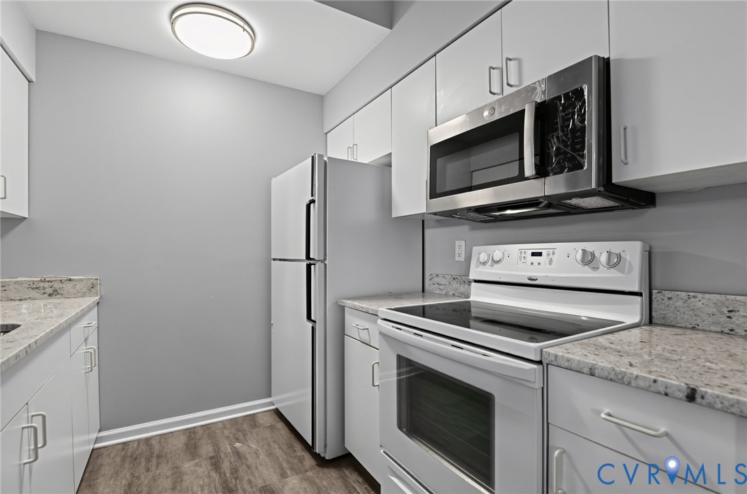 Kitchen featuring white cabinetry, stone-surface countertops, wood-finish flooring, and stainless steel microwave