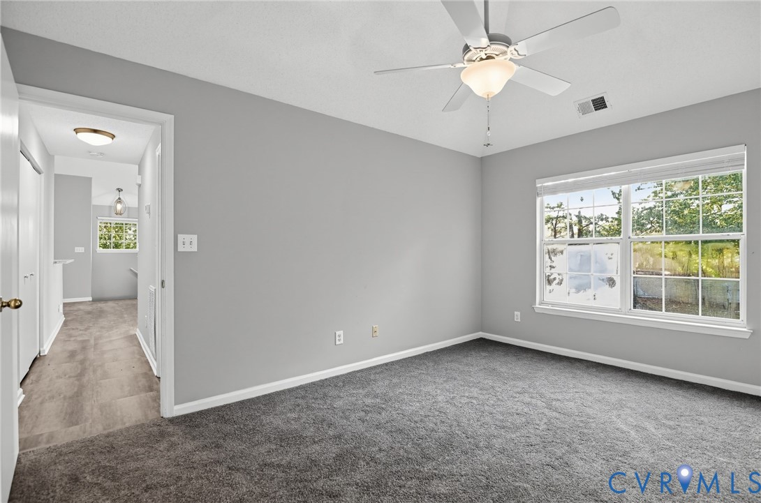 Neutral wall finishes, neutral carpeting, ceiling fan with integrated light fixture, and large-pane window with horizontal blinds
