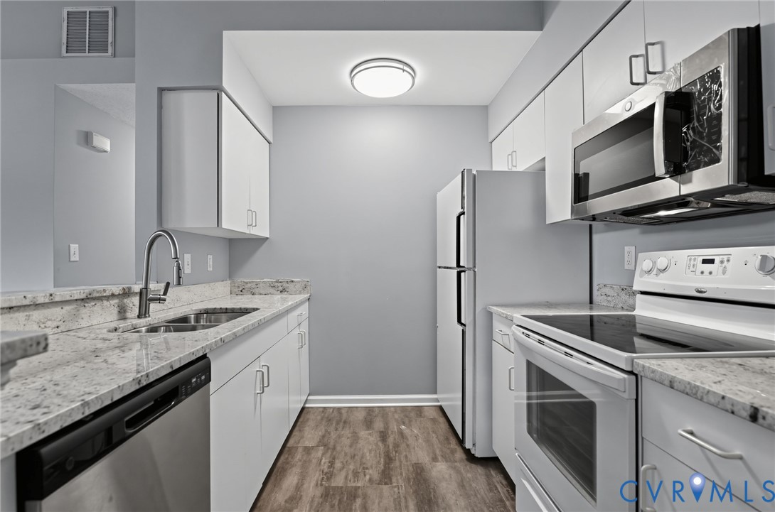Kitchen featuring stone-finish countertops, stainless steel appliances, wood-finish flooring, white cabinetry, and an under-mount double-basin sink with a gooseneck faucet
