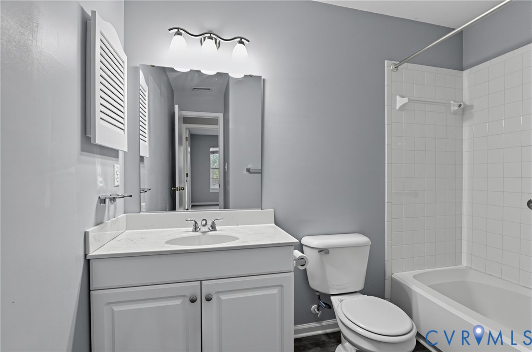 Bathroom featuring a white vanity cabinet with an integrated sink, stone-composite countertop, three-light fixture, wall-mounted shuttered cabinet, and a shower-tub combination with white tile surround