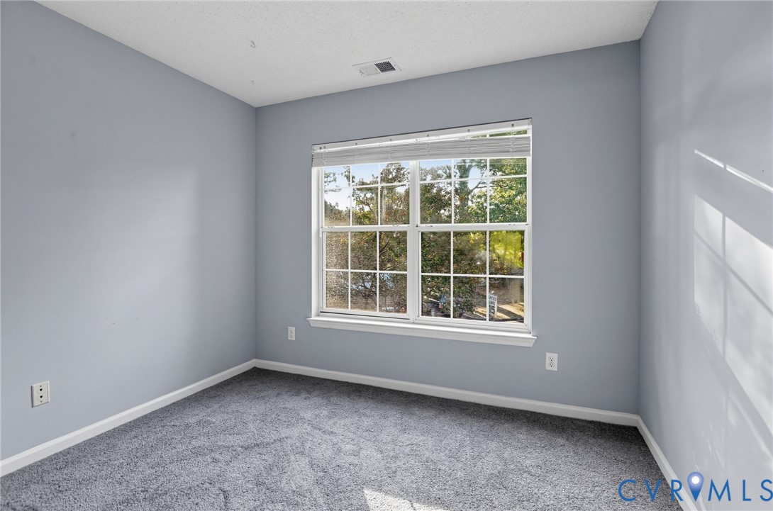 Neutral-toned interior space featuring gray carpeting, soft gray wall paint, and a multi-pane window with horizontal blinds