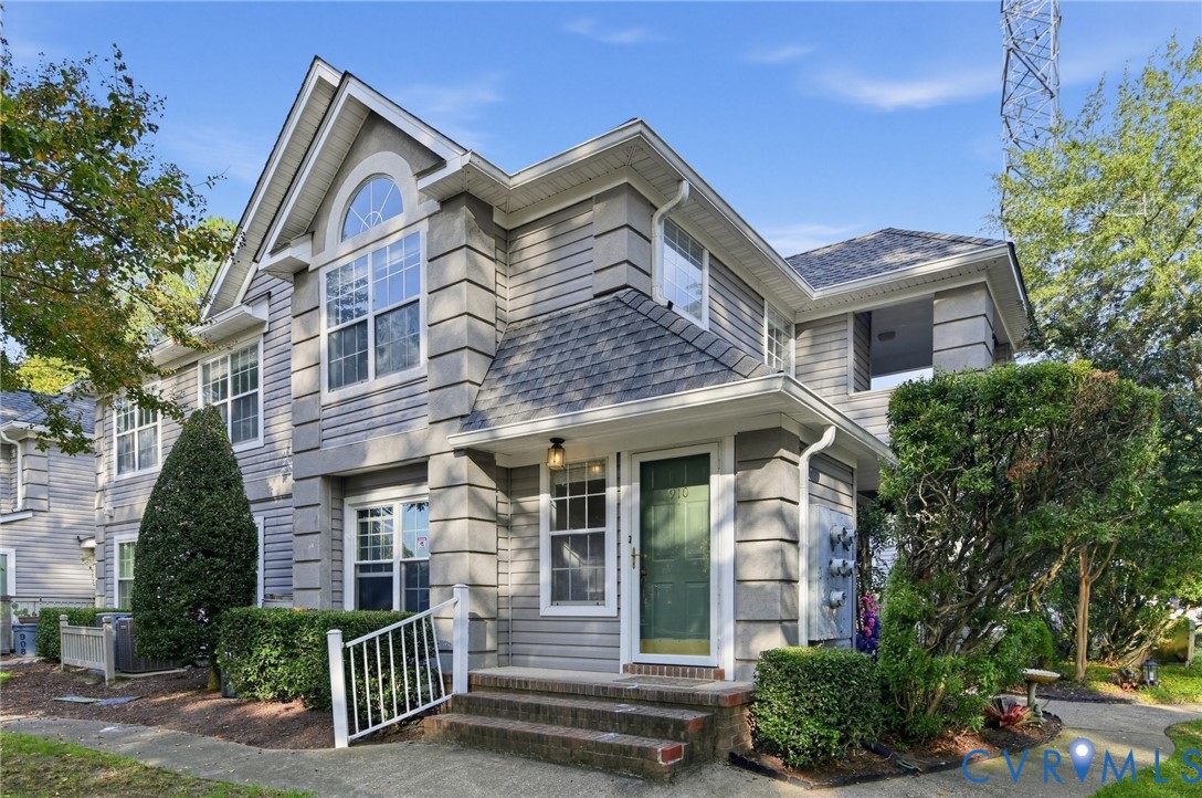 Multi-story exterior featuring gray lap siding, decorative corner quoins, an arched window, a gabled roofline, and a covered front entry with brick steps