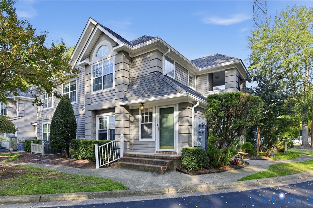 Multi-level residence featuring gray lap siding, corner quoins, an arched window, and a covered entryway with a brick-stepped stoop
