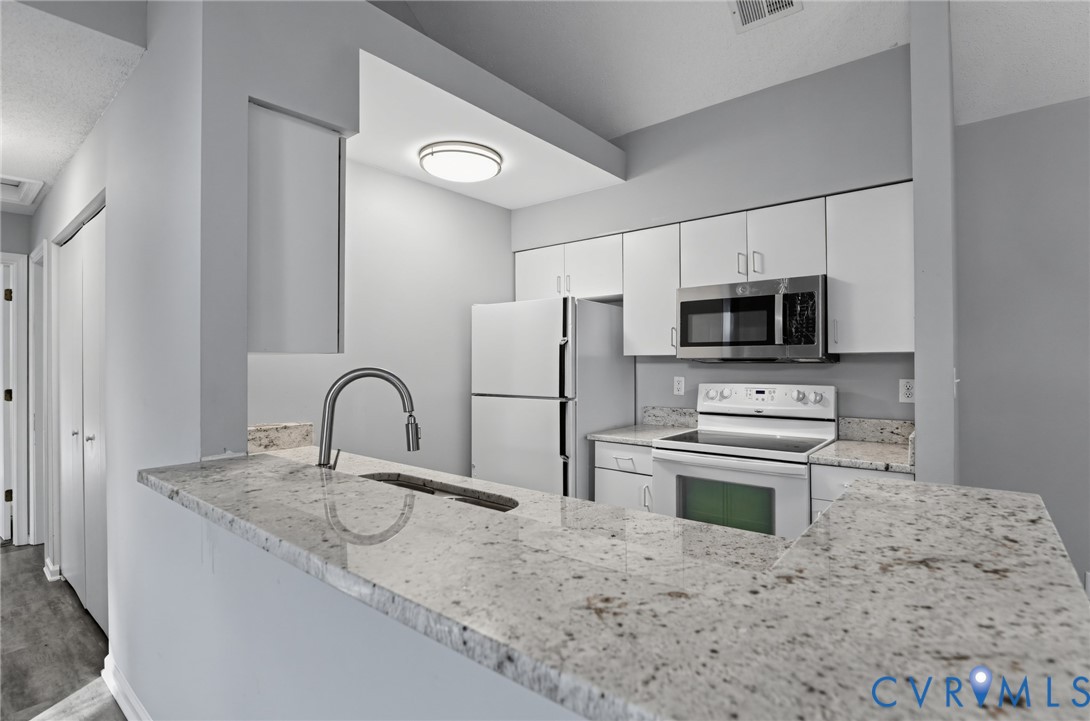 Kitchen featuring stone-finish countertops, a stainless steel undermount sink with a gooseneck faucet, white cabinetry, and stainless steel microwave