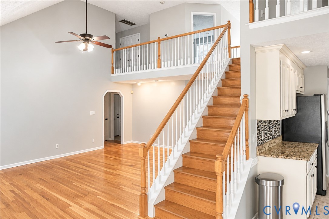 Vaulted ceiling, wood-finish flooring, staircase with a wood handrail and white balusters, overhead ceiling fan, and built-in cabinetry with a stone-finish countertop Vaulted ceiling, wood-finish flooring, staircase with a wood handrail and white balusters, overhead ceiling fan, and built-in cabinetry with a stone-finish countertop