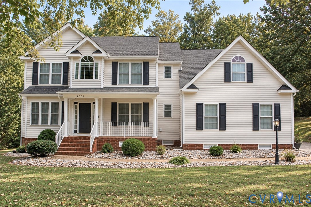 Two-story residence featuring light-colored horizontal siding, a brick-foundation facade, an arched window detail, decorative shutters, and an elevated front porch