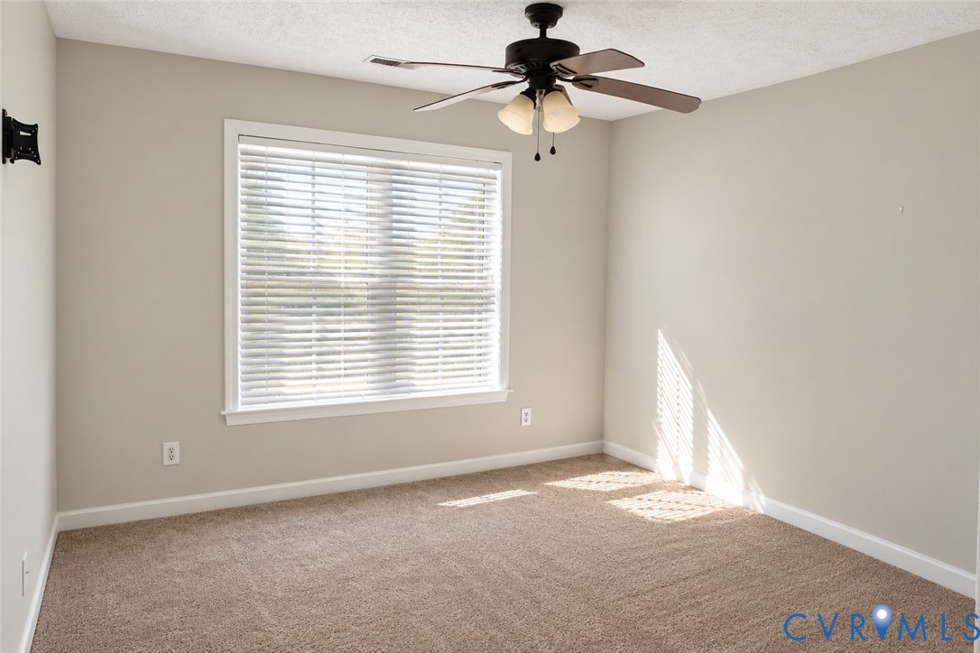 Neutral wall coloring, wall-to-wall carpeting, single-pane window with horizontal blinds, and a multi-bulb ceiling fan with an integrated light fixture