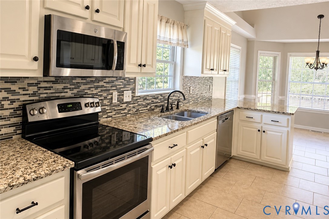 Kitchen featuring white cabinetry, stone-finish countertops, stainless steel appliances, a multi-tone tile backsplash, and tile flooring Kitchen featuring white cabinetry, stone-finish countertops, stainless steel appliances, a multi-tone tile backsplash, and tile flooring
