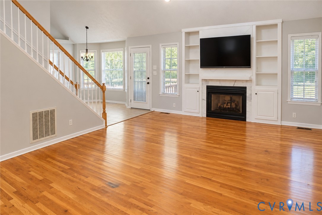 Open-concept living space featuring wood-finish flooring, vaulted ceilings, a fireplace with floor-to-ceiling built-in shelving, and a wood-railing staircase Open-concept living space featuring wood-finish flooring, vaulted ceilings, a fireplace with floor-to-ceiling built-in shelving, and a wood-railing staircase