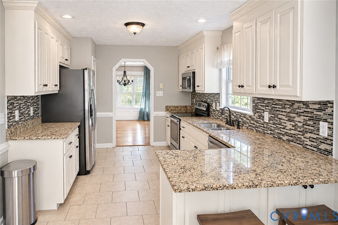 Kitchen featuring white shaker-style cabinetry, stone-finish countertops, decorative mosaic tile backsplash, stainless steel appliances, and ceramic tile flooring Kitchen featuring white shaker-style cabinetry, stone-finish countertops, decorative mosaic tile backsplash, stainless steel appliances, and ceramic tile flooring