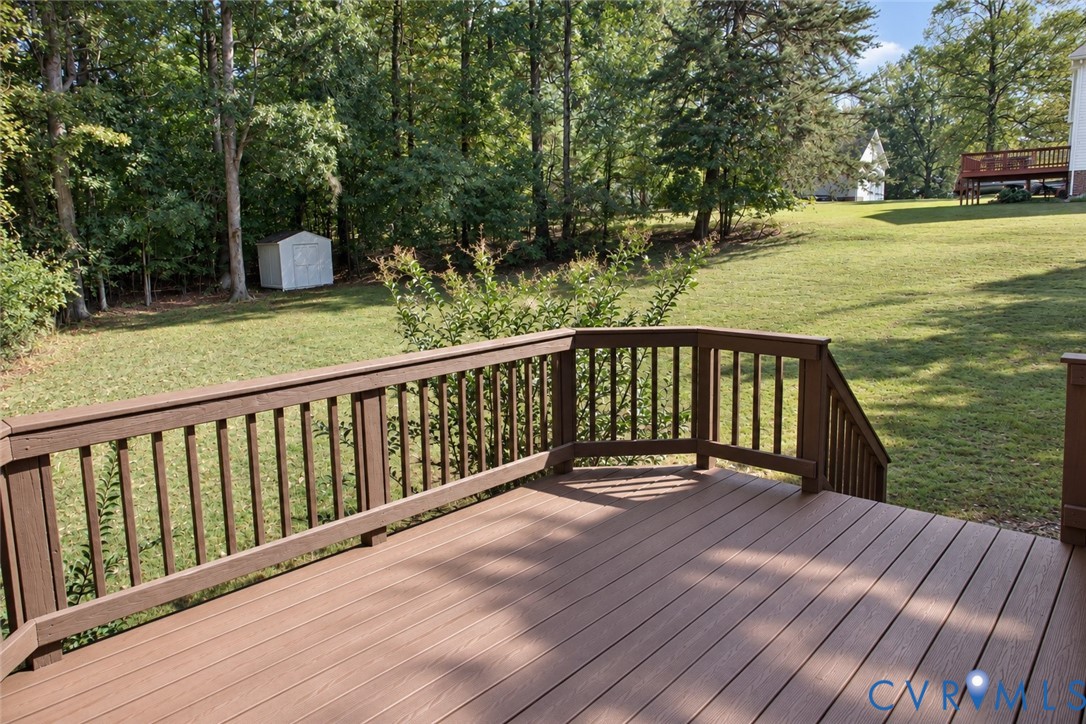 Elevated wood-finish deck with railings, expansive lawn, and mature perimeter trees