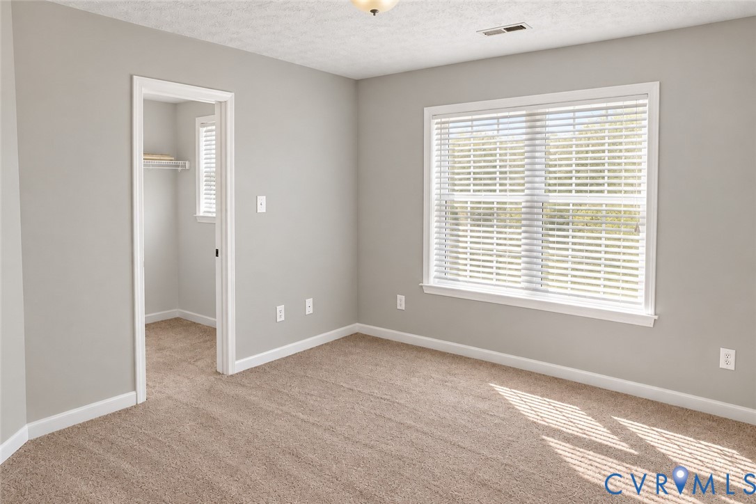 Neutral-toned interior walls featuring wall-to-wall carpeting, a large window with horizontal blinds, and a walk-in closet with built-in shelving