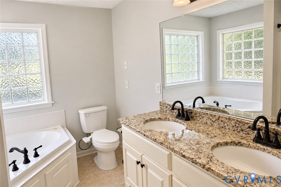 Dual-sink vanity with stone countertop and matte black fixtures, jetted soaking tub with tile surround, and privacy-glass windows