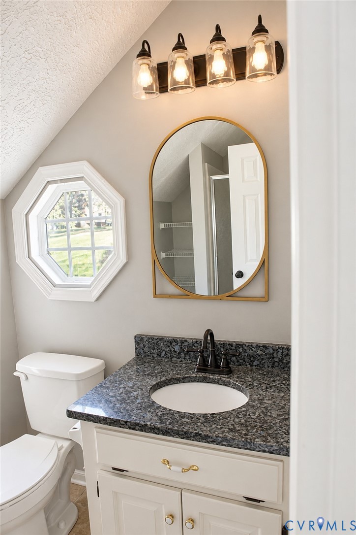 Vanity featuring a stone-composite countertop with an integrated basin, arched gold-framed mirror, four-light glass fixture, and an octagonal window