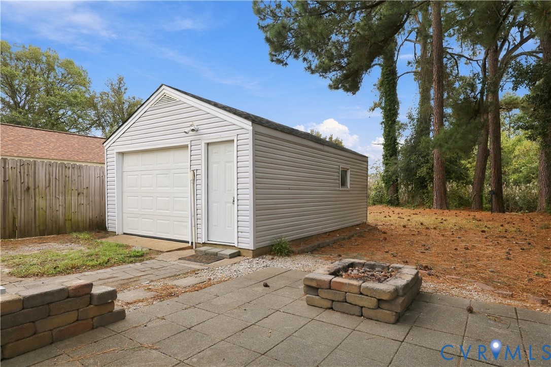 Detached single-car garage featuring vinyl siding, a paved patio, and a stone-style fire pit