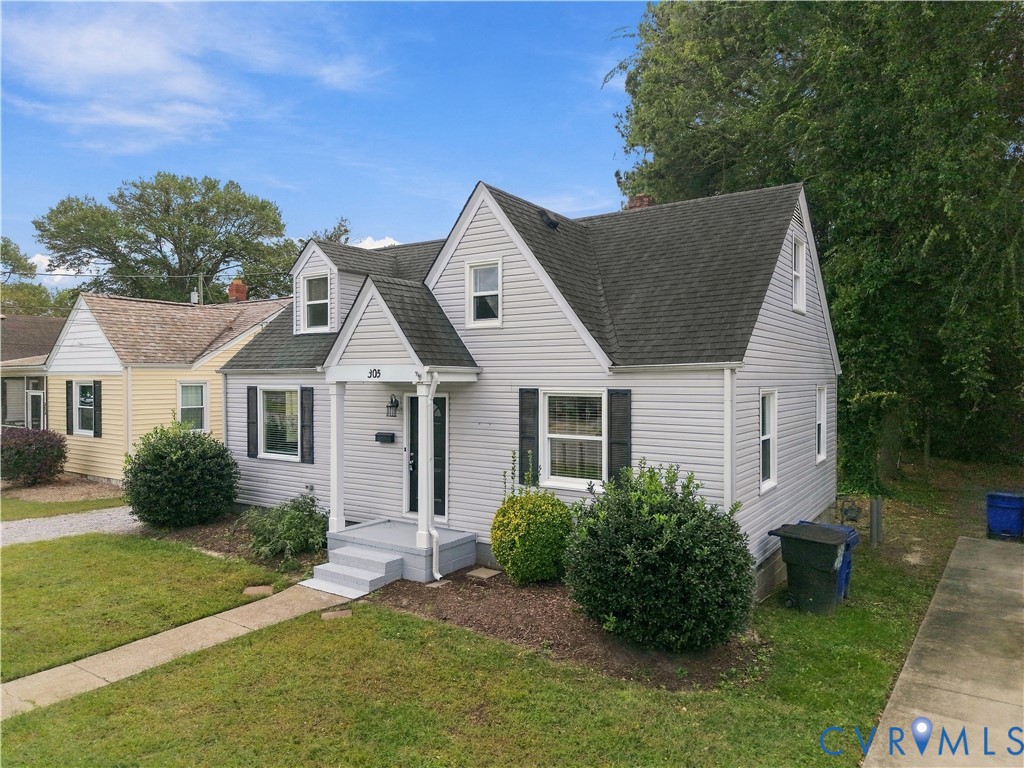 Cape Cod-style residence featuring light gray vinyl siding, a steep-pitched roof with prominent gables, decorative window shutters, and a covered front entryway