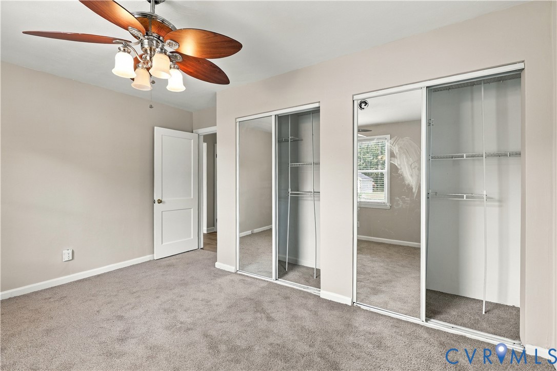 Room featuring neutral-toned carpeting, dual closets with sliding mirrored doors, and a ceiling fan with integrated multi-light fixture
