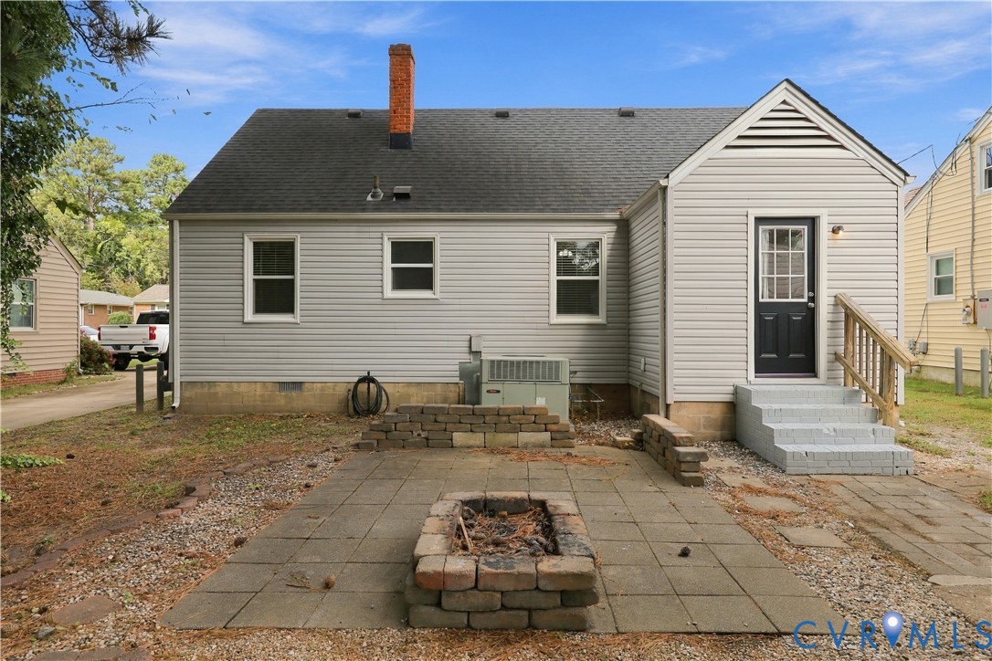 Exterior of home featuring vinyl siding, a brick chimney, a stone paver patio, and a built-in stone fire pit