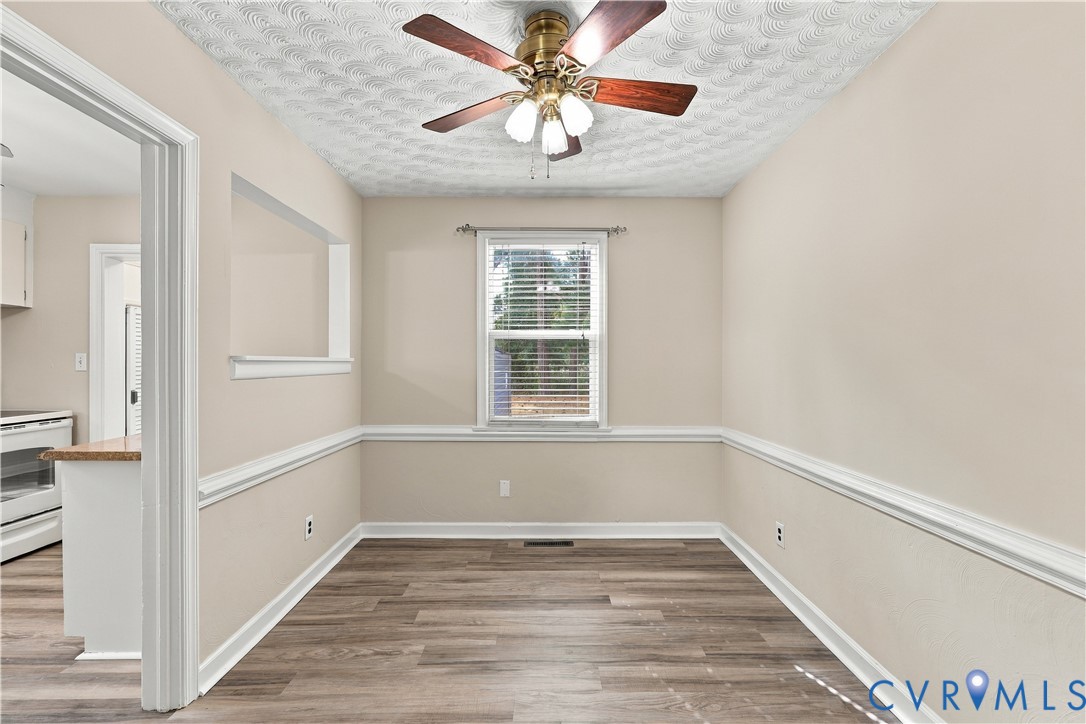 Wood-finish flooring, chair rail molding, ceiling fan with integrated lighting, textured ceiling, and an interior pass-through opening