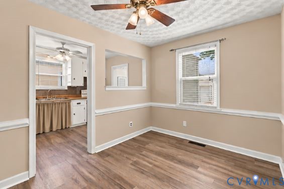 Room featuring wood-finish flooring, chair rail molding, a ceiling fan with integrated light fixture, and an interior pass-through opening
