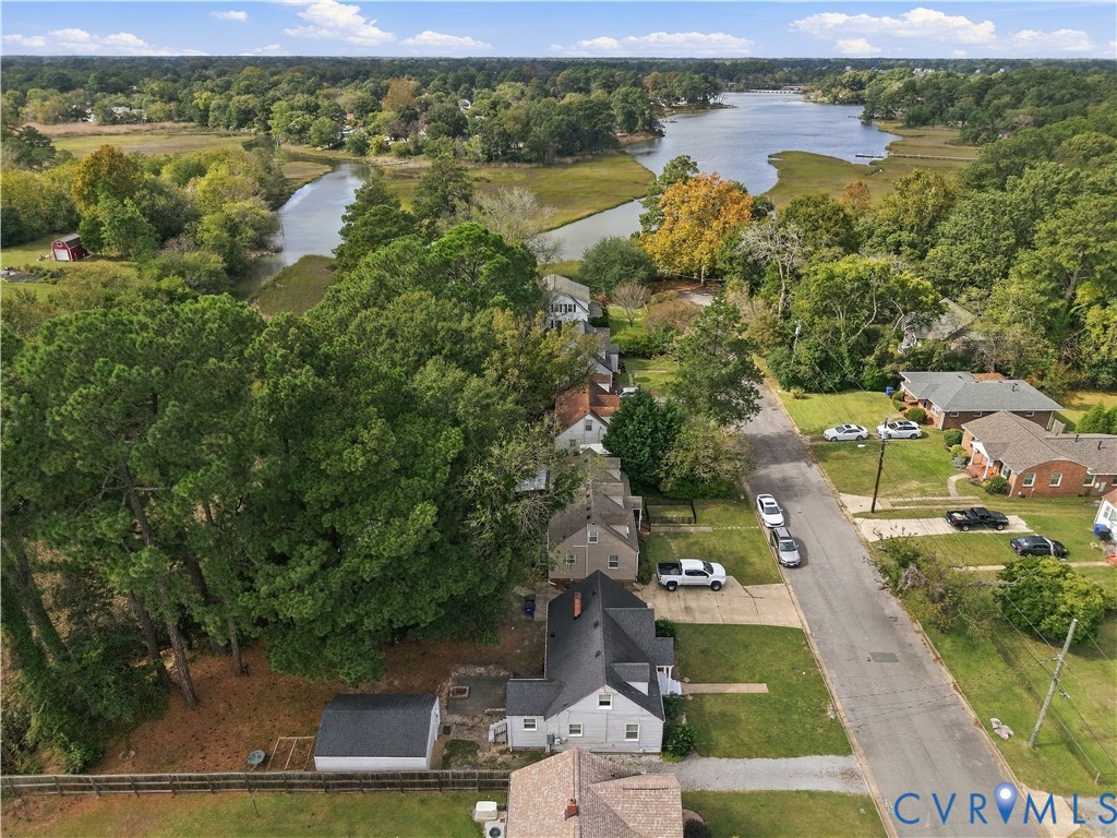 Aerial perspective featuring a residential lot with mature trees and a detached structure, situated within proximity to coastal waterways and dense natural foliage