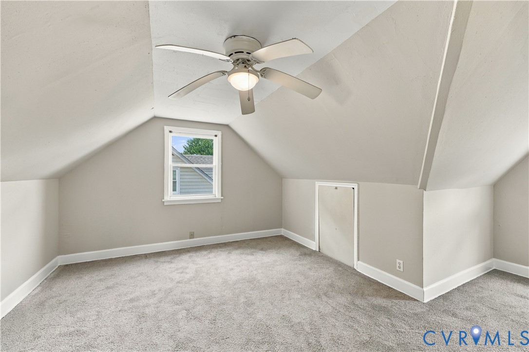 Vaulted ceilings featuring a central white ceiling fan with integrated lighting, neutral wall finishes, plush wall-to-wall carpeting, a single-pane window, and an integrated access panel for attic storage